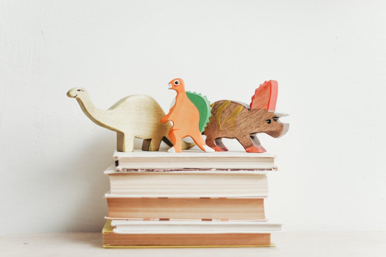 3 dinosaur toys on top of stacked books
